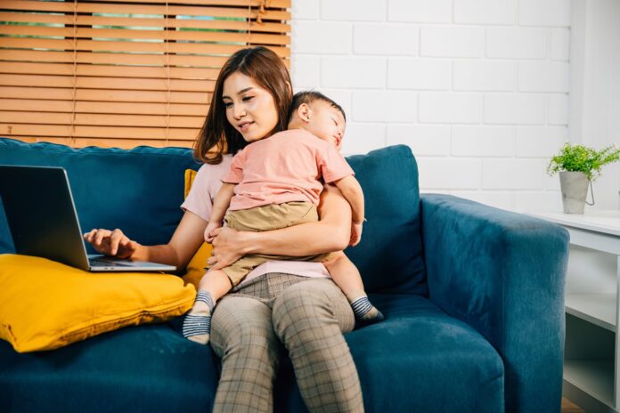 Mamma al computer tenendo in braccio il figlio che dorme