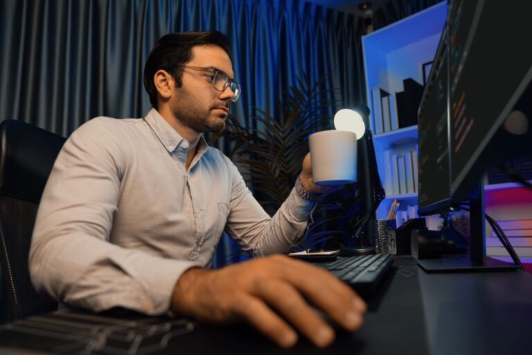 Uomo beve un caffè mentre lavora in casa davanti al computer