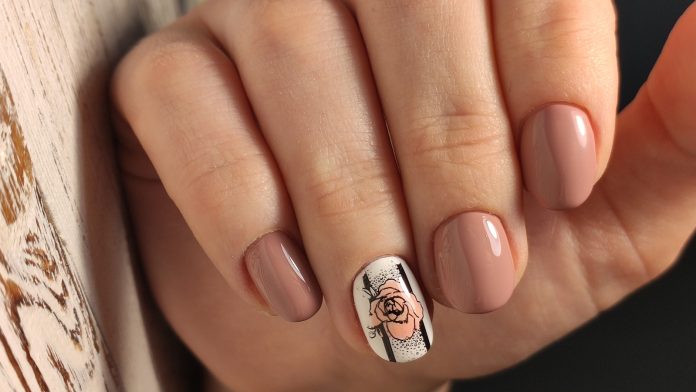 Mano donna, smalto nude e design con foglia autunnale sull'unghia dell'anulare