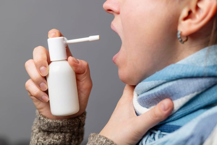 Una donna spruzza uno spray in bocca per alleviare i sintomi del mal di gola