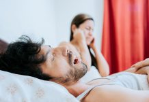 Cosa fare per non russare: consigli per smettere subito Un uomo e una donna a letto, il primo russa e la seconda si tappa le orecchie